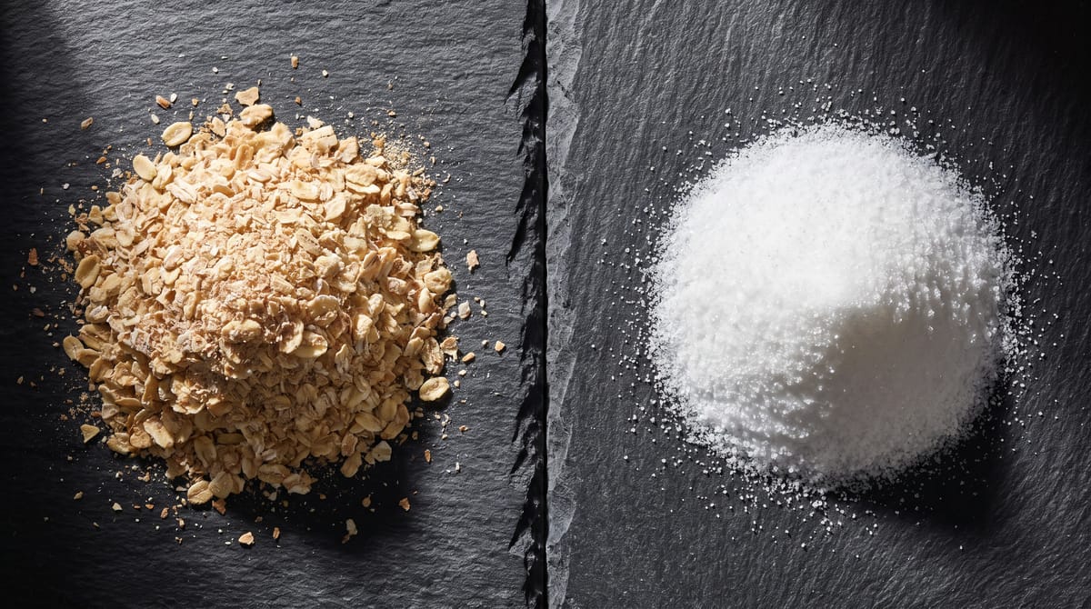 Golden wheat germ flakes next to a heap of pure white crystalline powder on dark slate